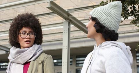 Two women chatting at urban plaza wearing scarf beanie and eyeglasses