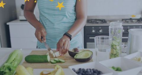 Woman slicing cucumber and avocado on wooden board wearing fitness tracker for healthy meal prep