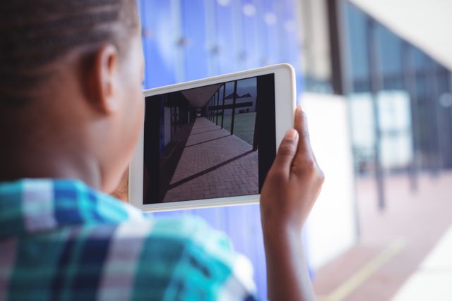 Schoolboy using a digital tablet to photograph a corridor at school during a sunny day. Ideal for use in educational materials, technology in education promotions, and modern learning environments.