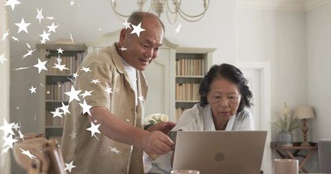 Senior couple collaborating on laptop at home pointing and navigating digital tasks