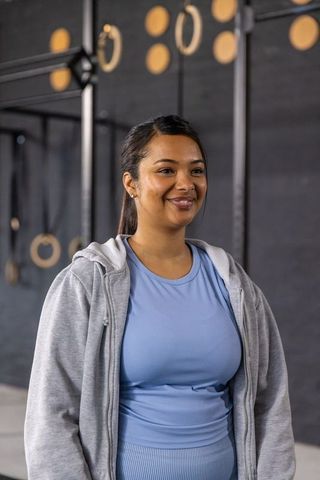 Confident asian woman smiling in activewear at industrial gym with wooden rings and rig