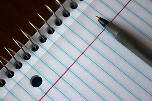 Close-up of a spiral notebook with lined paper and a pen lying on a table. Ideal for educational and business presentations, illustrating note-taking concepts, or decorating school and office-related articles.