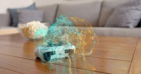 Glowing wireless game controller releasing teal and amber energy smoke on coffee table