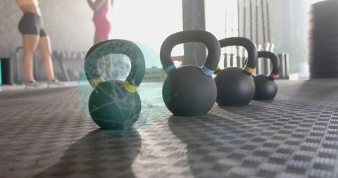 Sitting kettlebell with yellow band on gym floor, backlit workout with women standing