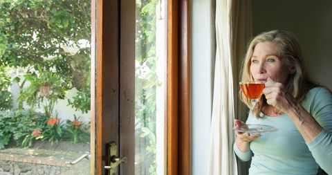 Senior Woman Sipping Tea by Garden View Door in Relaxing Home Atmosphere