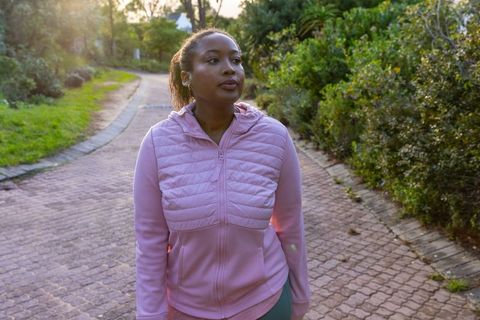 African american woman walking in park with earbuds enhancing fitness routine