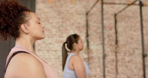Women practicing mindful breathing and warmup at industrial gym with brick wall and rig