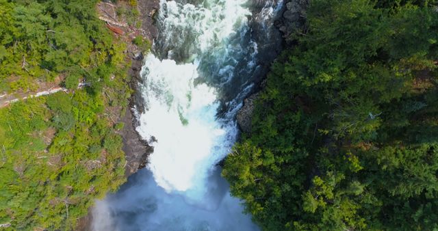 Aerial view of a powerful waterfall surrounded by lush greenery, with copy space. The cascading water creates a misty atmosphere, emphasizing the natural beauty and force of the landscape.