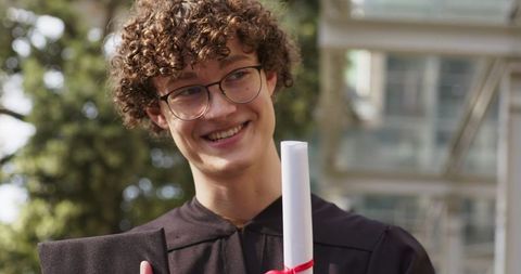 Smiling male graduate holding diploma and cap, celebrating on university campus