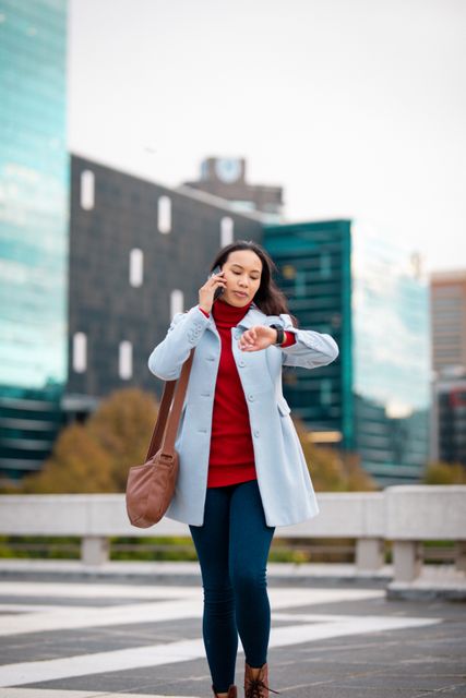 Asian woman crossing road, talking by smartphone and checking smartwatch. out and about in the city.