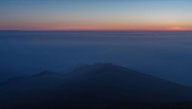 Dawn mist rolling across layered mountain ridges, silhouetted peaks piercing foggy valley