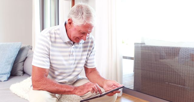 Senior man using tablet for online activities at home recaps the concept of elderly people embracing technology for personal or educational purposes. Could be used in articles or campaigns on digital literacy for seniors or advertising products and services for older adults.