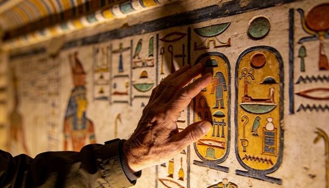 Senior hand touching painted egyptian cartouches in tomb, exploring hieroglyphic relief