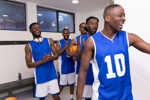 African american basketball team celebrating victory in locker room wearing blue jerseys