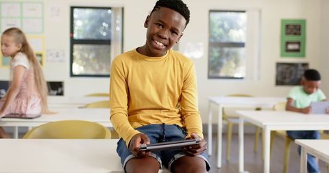 Smiling african american boy using tablet, learning technology in sunlit elementary classroom