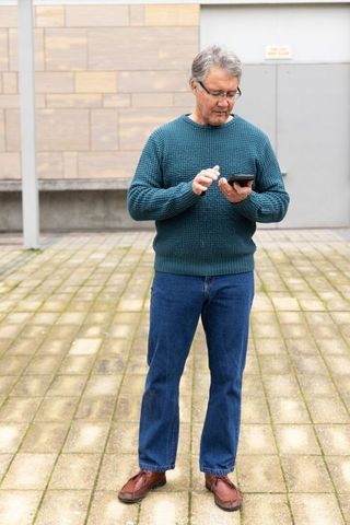 Senior man standing in urban courtyard using tablet touchscreen, casual tech use and connectivity