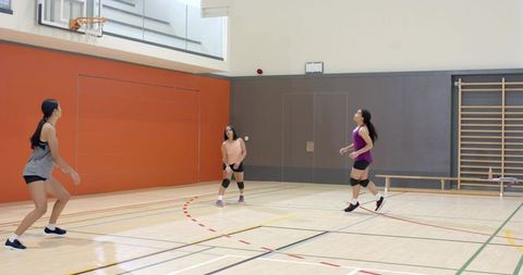 Diverse female teammates practicing volleyball drills on school gym court wearing knee pads