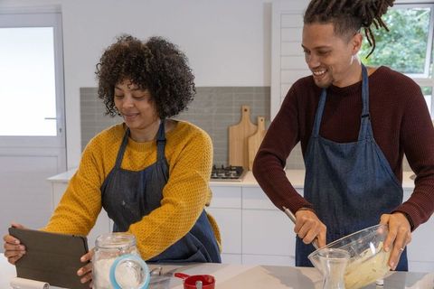 Couple baking together in bright modern kitchen using tablet for recipe, whisking batter