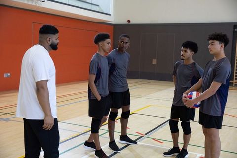 Coach leading diverse male teenage volleyball team in indoor gym during practice drill