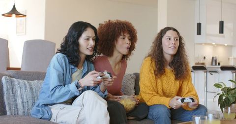 Three Friends Playing Video Games, Sharing Popcorn and Reacting on Modern Open-Plan Sofa