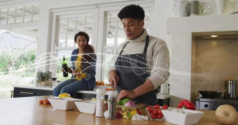Couple cooking in modern bright kitchen at island, man chopping vegetables woman pouring wine