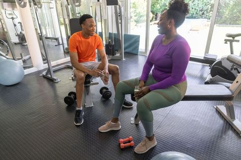 African american workout partners chatting while resting on gym bench in vibrant activewear