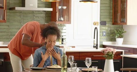 Man gifting necklace to woman at home in kitchen scene