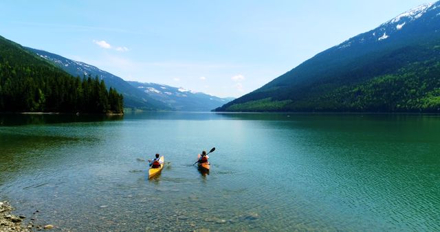 Two kayakers paddling in clear, tranquil lake surrounded by lush green mountains and forest, perfect for outdoor adventure, summer holidays, travel brochures, and promoting eco-friendly activities.