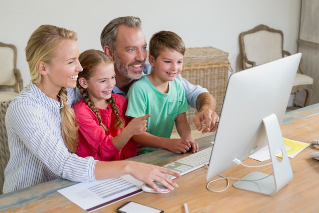 Family gathered around computer, smiling and pointing at screen. Ideal for depicting family bonding, technology use, online learning, and modern family lifestyle.