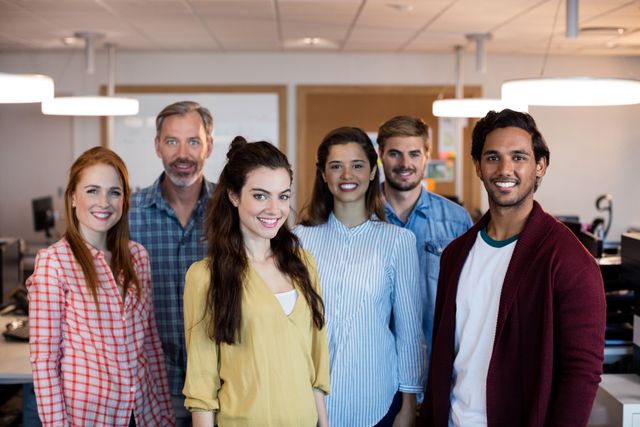 Group of diverse colleagues smiling and standing in a modern office. They are posing together, representing teamwork and collaboration in a professional environment. Ideal for promoting business, teamwork, startup culture, and modern office settings.