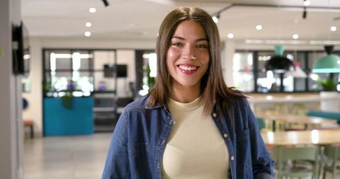 Smiling young woman standing in modern open-plan coworking space wearing denim shirt