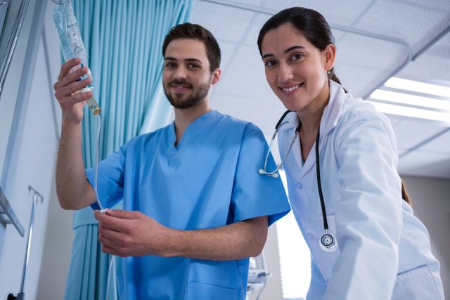 Medical professionals, including a doctor and a nurse, are adjusting an IV drip in a hospital setting. Both are smiling and appear focused on their task, showcasing teamwork and patient care. This image can be used for healthcare-related content, medical websites, hospital brochures, or educational materials about medical procedures and teamwork in healthcare.