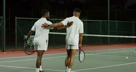 Tennis duo walking on night court in white uniforms showing teamwork and sportsmanship