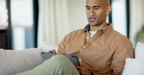 Mature man relaxing on sofa using tablet in sunlit modern living room