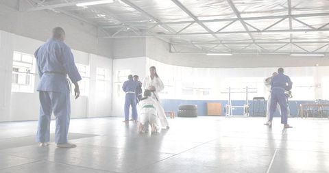 Teen female grappling in white gi with green belt practicing martial arts in bright dojo