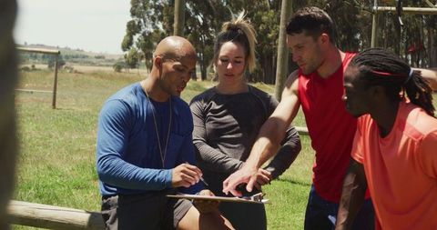 Diverse group discussing performance with coach at obstacle course