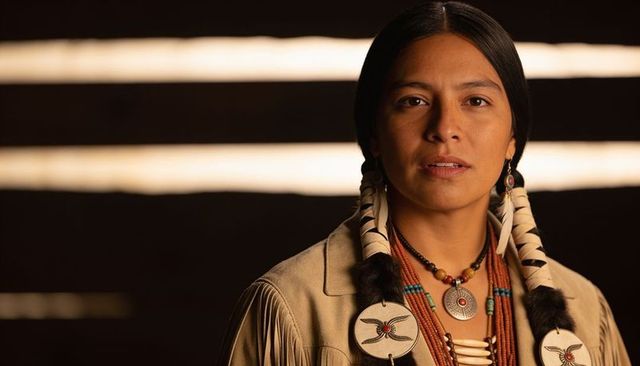 Warm studio portrait woman wearing buckskin fringed jacket, braided hair, beaded medallion