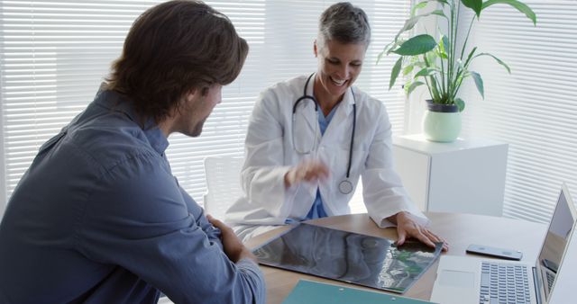 Doctor and patient reviewing x-ray results together in a modern office environment. The doctor, wearing a white coat and stethoscope, appears engaged and explaining medical details to the patient. The scene suggests concepts of healthcare, medical advice, diagnosis, and professional consultation. Ideal for use in articles about health, patient care, medical consultations, diagnostics, clinic settings, and doctor-patient relationships.