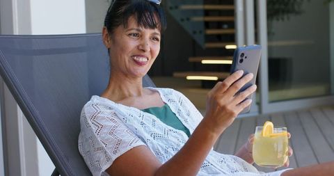 Woman relaxing on terrace with lemonade while video calling on smartphone