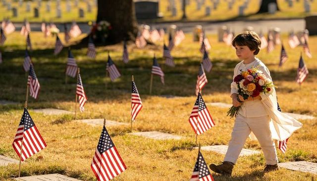 Child walking with bouquet through veteran cemetery lined by american flags at golden hour