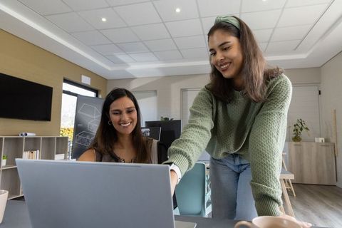 Female colleagues collaborating over laptop in modern bright office with coffee and teamwork
