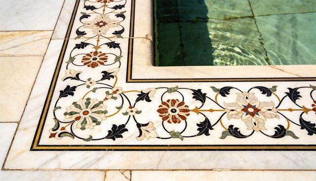Ornate marble border framing pool with floral pietra dura inlay and sunlight reflections