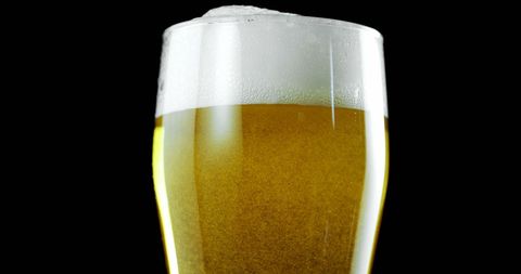 Close-up Glass of Beer with Foamy Head Against Black Background