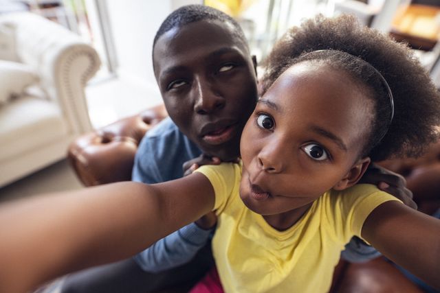 Portrait of african american playful girl puckering lips and taking selfie with father making faces. Unaltered, family, togetherness, childhood, enjoyment, lifestyle and home concept.