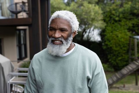Senior african american man smiling and standing in backyard wearing green sweatshirt