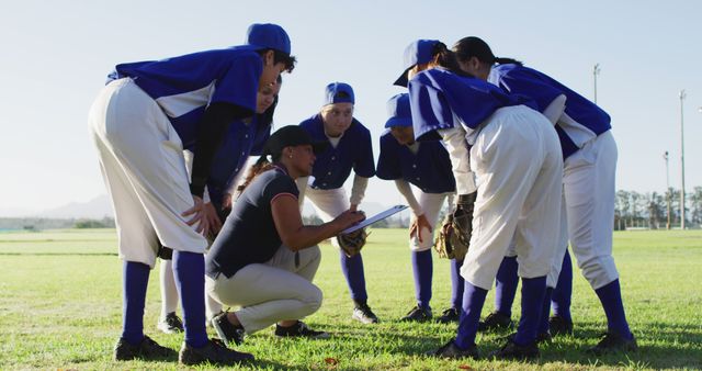 Diverse group of female baseball players huddled around female coach, squatting and talking on pitch. female baseball team, sports training and game tactics.