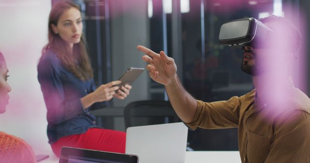 Team members use virtual reality technology during a collaborative meeting in a modern office environment. One team member is engaged with a VR headset while others observe and interact. Great for illustrating technological innovation, teams collaborating in diverse digital environments, or modern business practices in professional settings.