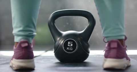 African american woman standing over 5kg kettlebell in mint leggings purple sneakers