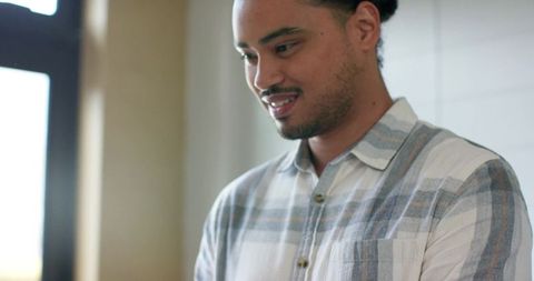 Mid-adult man standing by window smiling in casual plaid shirt natural daylight portrait