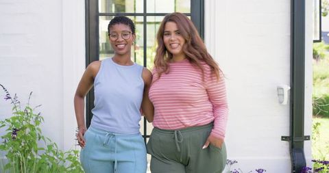 Multicultural women smiling at home entrance embracing friendship in casual loungewear